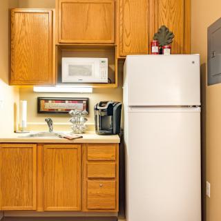 A compact kitchen setup with wooden cabinets, a white refrigerator, microwave, and a coffee maker.