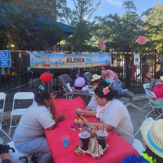 A vibrant community gathering with people enjoying food and drinks under a sunny sky.