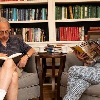 Two people sitting in armchairs, absorbed in their reading in a cozy library setting.
