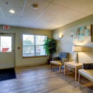 A cozy lobby area with chairs, plants, and a lamp, featuring natural light from a window.