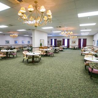 A spacious dining area with chandeliers, featuring several tables and chairs on a carpeted floor.