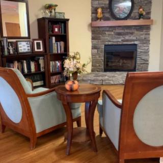 A cozy living room setup featuring a pair of elegant chairs facing a stone fireplace, surrounded by a bookshelf and decor on wooden flooring.