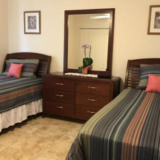 A cozy bedroom featuring two twin beds with striped bedding, a dresser with a mirror, and decorative elements.