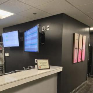 A modern office reception area with wall-mounted monitors and a desk displaying certificates.
