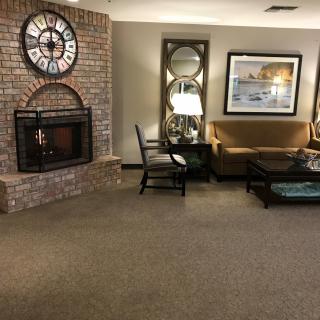 A cozy living room featuring a brick fireplace, large clock, and comfortable seating arrangement.