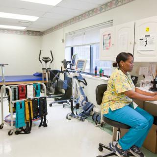 A nurse working at a desk in a medical office with exercise equipment.