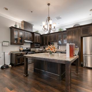 A modern kitchen featuring an island with dark wood cabinets, stainless steel appliances, and a chandelier.