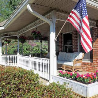 A cozy front porch with an American flag, wicker seating, and vibrant flowers.
