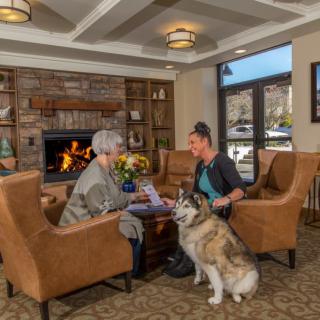 Two people having a conversation by the fireplace with a dog in a cozy living room.