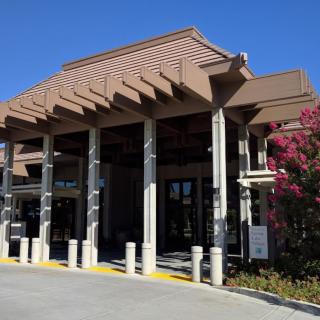 A building entrance with prominent columns and a pergola-style roof, surrounded by landscaping.