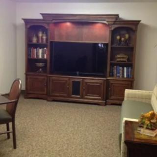 A cozy living room with a large wooden entertainment center, featuring a television and bookshelves.