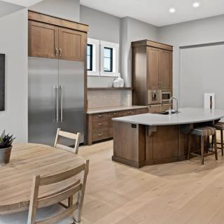 A modern kitchen featuring wood cabinets, a large island counter, and stainless steel appliances, seamlessly connected to a dining area.