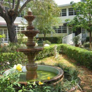 A serene garden with a decorative fountain and lush greenery in front of a building.