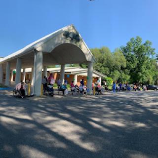 A sunny day at a spacious outdoor area with people gathered near a building surrounded by trees.