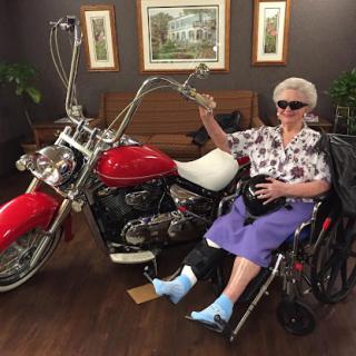 An adventurous elderly woman enjoys a moment next to a stylish red motorcycle, showcasing her vibrant spirit.