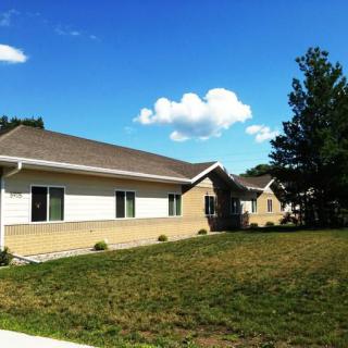 A single-story residential building with a grassy lawn under a clear blue sky.