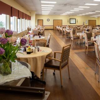 An empty dining room with set tables, decorated with vases of flowers and a wooden floor.