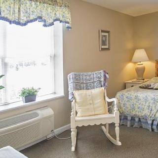 A cozy bedroom with a rocking chair near a window, showcasing soft lighting and decorative elements.