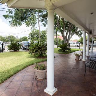A peaceful outdoor porch with white columns, greenery, and a tiled walkway.