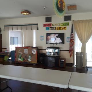 A view of a community room featuring tables and a television, decorated with colorful banners.