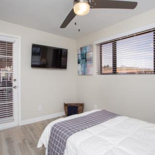 A modern minimalist bedroom with a ceiling fan, wall-mounted television, and window blinds.
