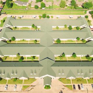 Aerial view of a large building complex with a green roof and surrounding parking areas.
