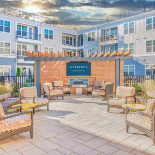 A modern outdoor patio with comfortable seating and a fireplace, situated within an apartment complex.