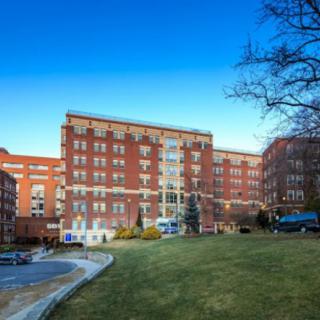 A large brick hospital building with manicured lawns and clear blue sky.