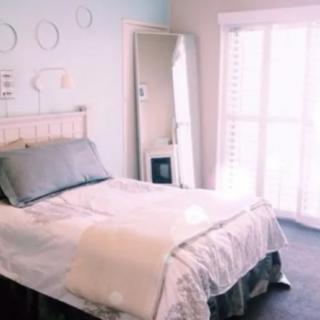 A cozy, well-lit bedroom with a neatly made bed and a full-length mirror.
