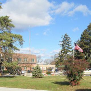 An outdoor scene featuring a building surrounded by trees, an American flag, and a clear sky with scattered clouds.