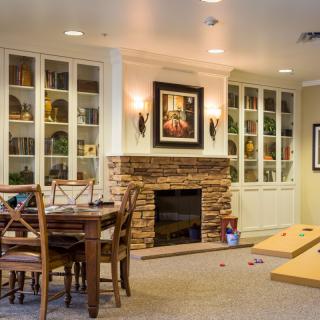 A cozy living room with a fireplace and built-in bookshelves, featuring a dining table and a cornhole game set on the carpet.