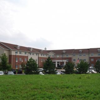 A large hospital building with a parking lot and surrounding greenery under a cloudy sky.