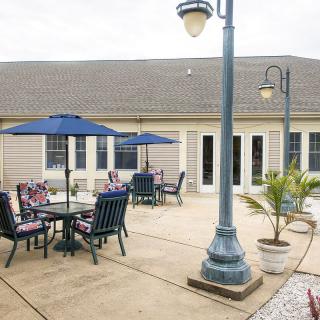A peaceful outdoor patio area with tables, chairs, and umbrellas surrounded by lamp posts and potted plants.