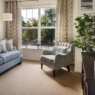 A cozy living room featuring a sofa, armchair, and large window with patterned curtains.