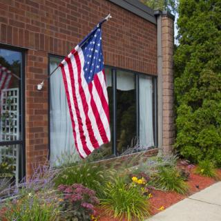 An American flag displayed outside a brick building surrounded by a landscaped garden.