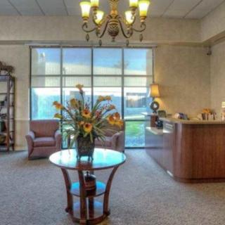 A welcoming office lobby featuring a glass table with flowers, comfortable armchairs, and a reception desk under an elegant chandelier.