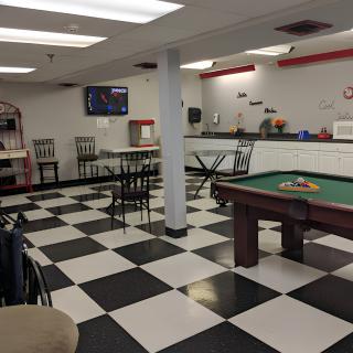 A game room with a checkered floor, featuring a pool table and cafe-style seating.