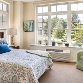 A cozy bedroom featuring a large window, patterned bedding, and comfortable seating.