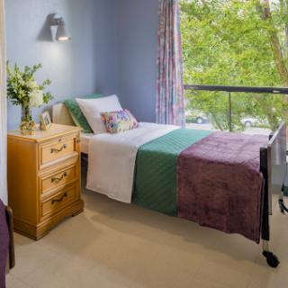 A cozy bedroom featuring a neatly made bed with a colorful quilt, natural light streaming in through the window, and tasteful decor.