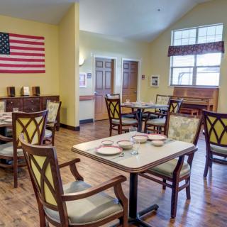 A cozy dining room with neatly arranged tables and chairs, featuring an American flag on the wall.