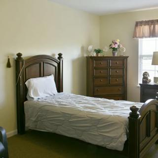 A cozy bedroom with a single bed and a wooden dresser, featuring a window for natural light.