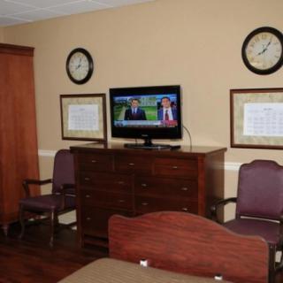 A hospital room with a television, chairs, and a dresser, displaying a news program.