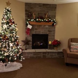 A cozy living room decorated for Christmas with a lit tree and a fireplace.