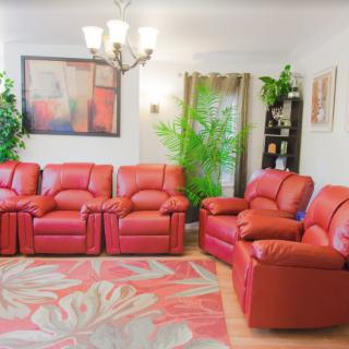 A cozy living room with red sofas, a decorative chandelier, and indoor plants.