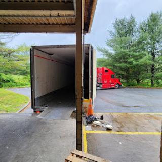 A red truck parked next to an empty trailer at a loading dock surrounded by trees.