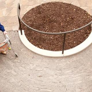 A worker sweeping a pathway next to a circular landscaped area.