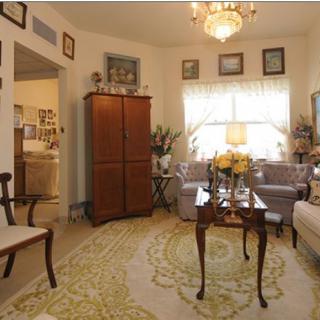 A cozy living room with traditional decor, featuring a sofa, armchairs, a wooden cabinet, and a chandelier.