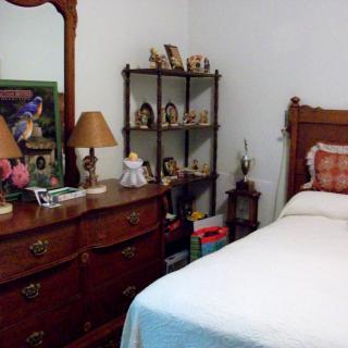 A cozy bedroom with a wooden dresser and mirror, adorned with lamps and decorative items, alongside a neatly made bed.