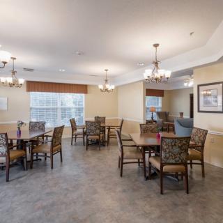 A spacious dining room with multiple tables and chairs, adorned with chandeliers and large windows.