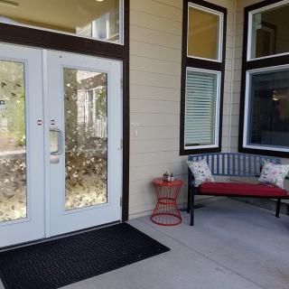 A welcoming entrance with glass doors, a black bench adorned with red and white pillows, and a black welcome mat.